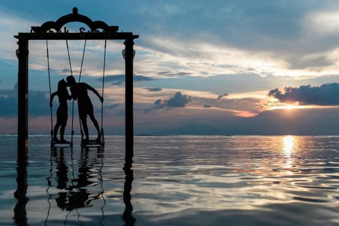 A couple on a swing over the water at sunset
