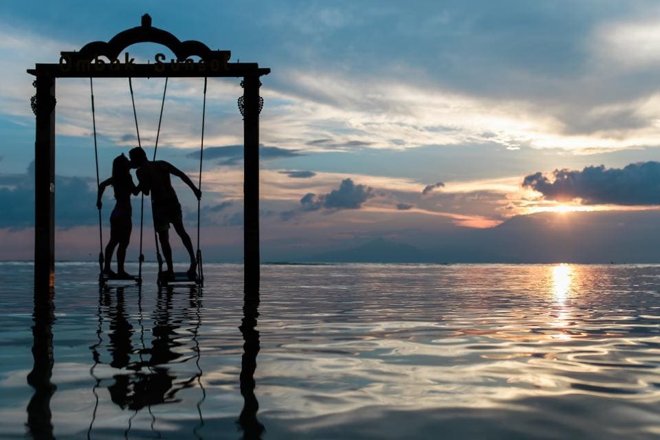 A couple on a swing over the water at sunset